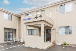 介護施設の玄関・車寄せ。白い外壁の建物で、看板と入口が見える